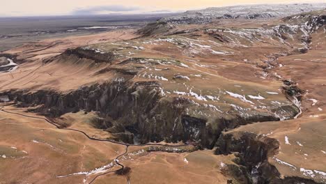 Breathtaking aerial view of Fjadrargljufur canyon in Iceland, cliffs, winding river and snowy landscape.