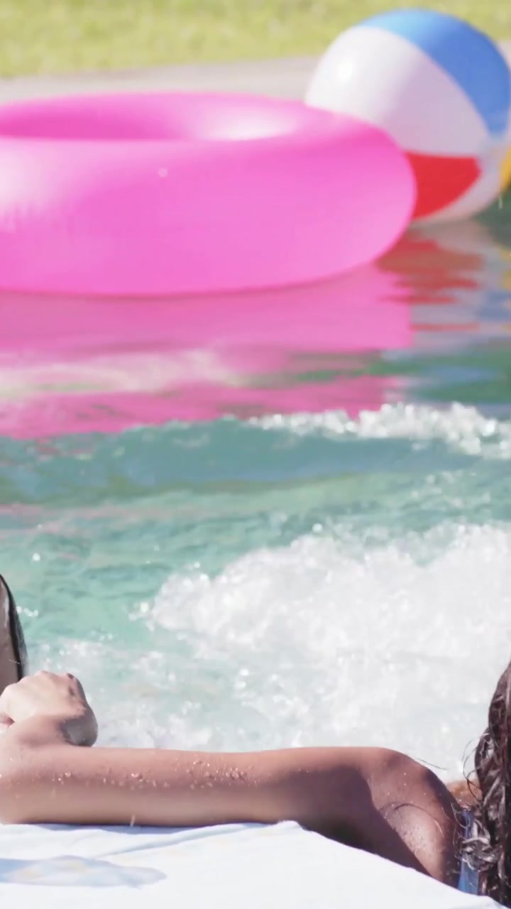 Vertical video: Splashing 3 women in swimwear at pool after arm reach cooling off with pink float