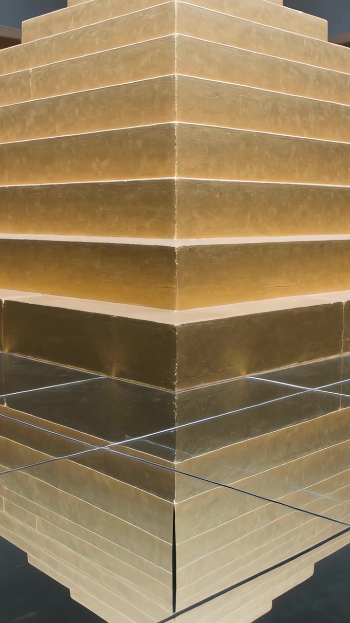 Vídeo vertical: Início do clipe, câmera inclinando para cima em museu, revelando o reflexo de uma escultura dourada.