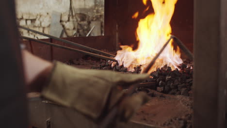 blacksmith tending forge fire and heating iron in workshop