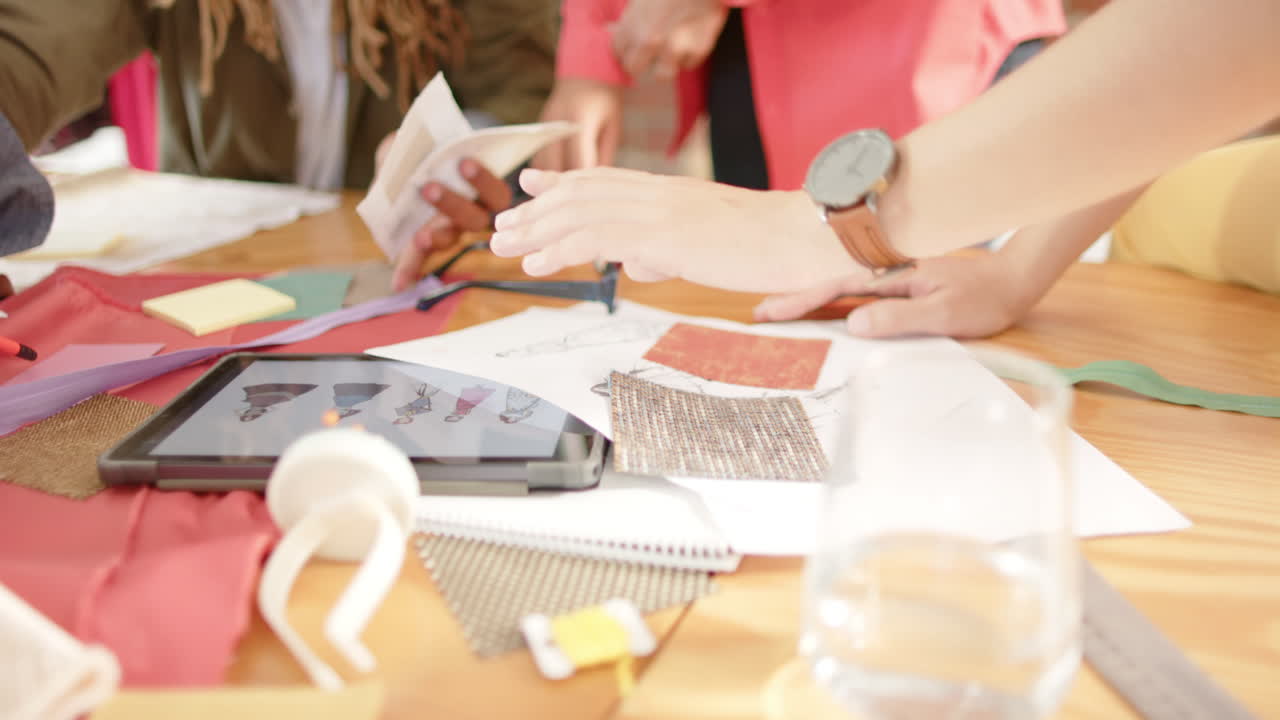 다양한 디자이너들이 패션 스튜디오에서 태블릿과 패션 그림으로 테이블에 앉아 일하고 있습니다.