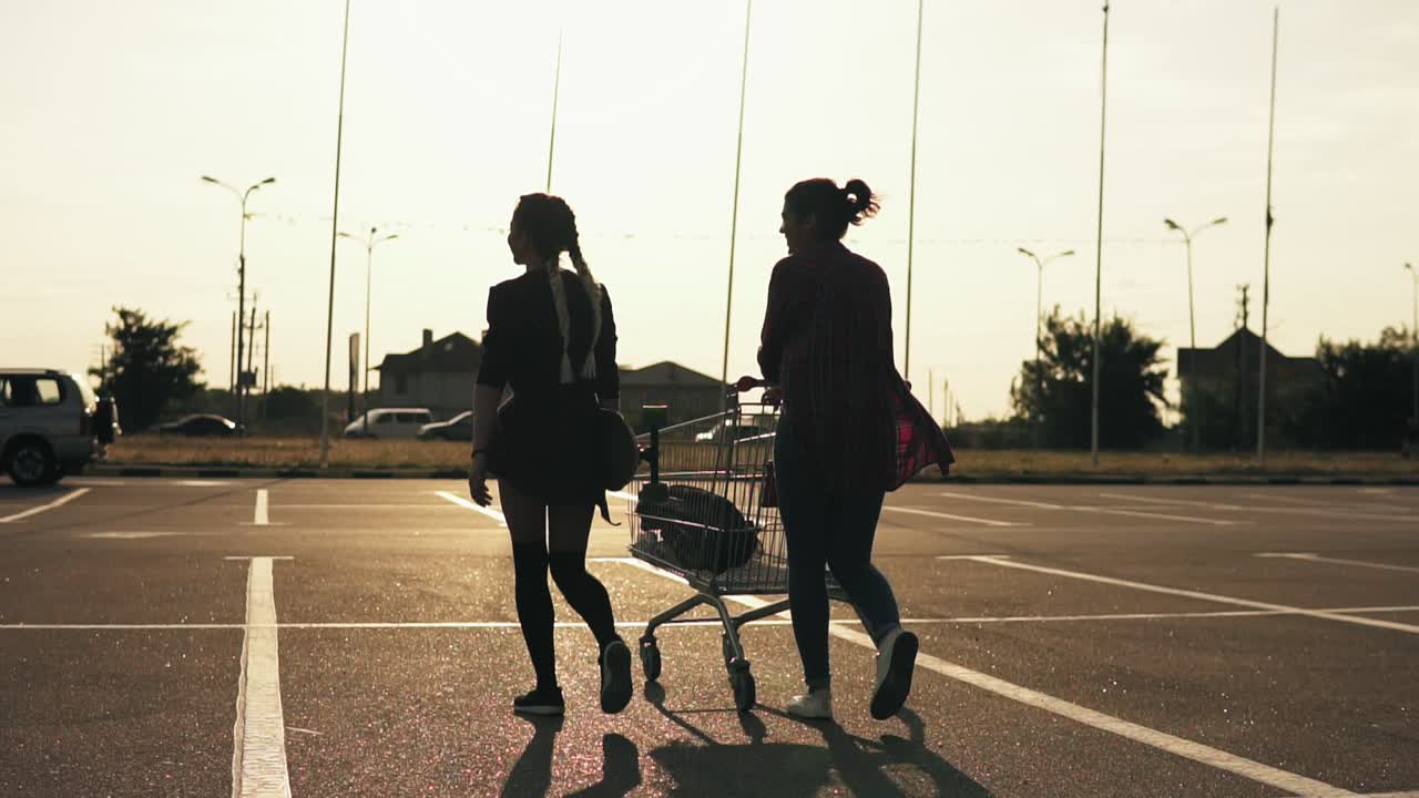 쇼핑센터 주차장을 걷고 있는 두 명의 매력적인 세련된 소녀의 뒷모습