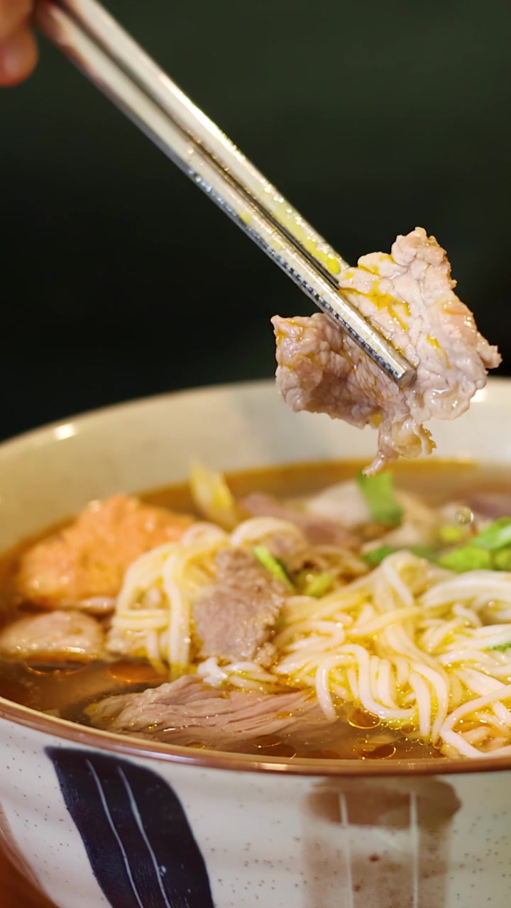 Cận cảnh một người đang gắp những lát thịt bò từ tô phở truyền thống Việt Nam bằng đũa kim loại.