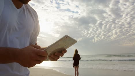 Low-Angle-Ansicht-Eines-Jungen-Kaukasischen-Mannes,-Der-An-Einem-Sonnigen-Tag-Am-Strand-Ein-Digitales-Tablet-Nutzt,-4K