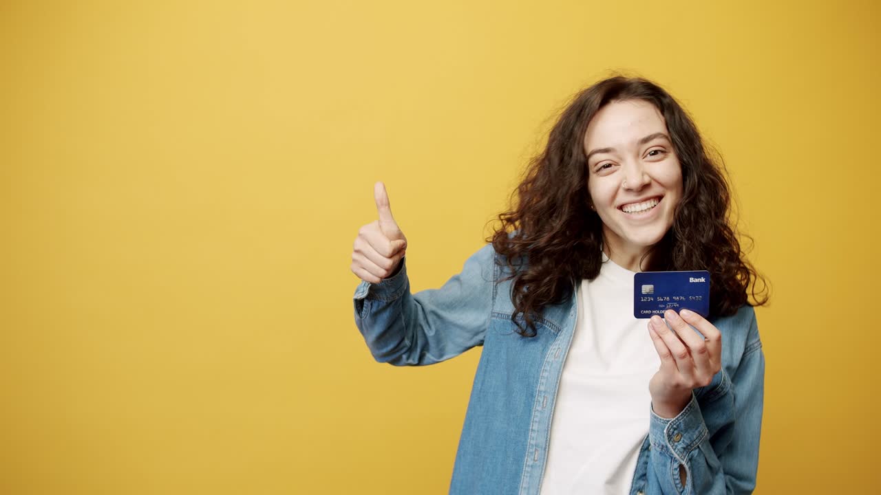 una chica recibe una tarjeta de crédito y ella está feliz, filmado estudio de fondo amarillo.