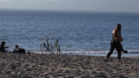 a young woman walking on the beach with water and various people in the background.