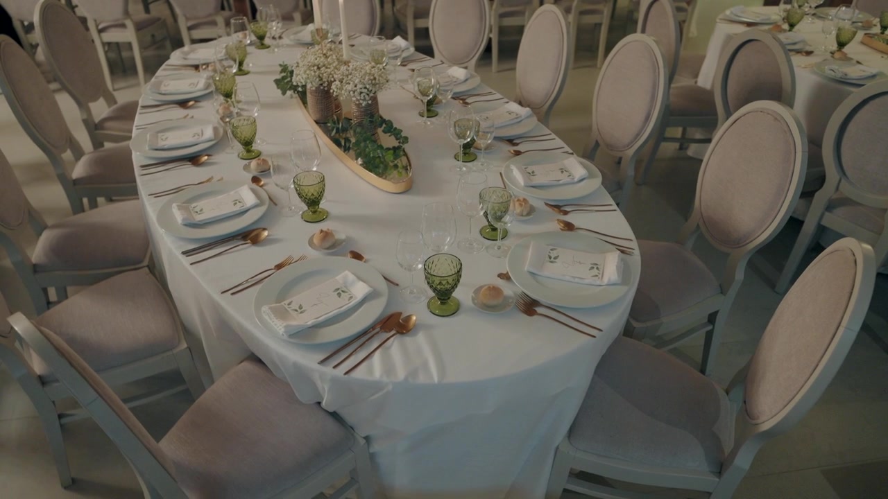 Elegant dining table set with white linens, green glasses, and a floral centerpiece.