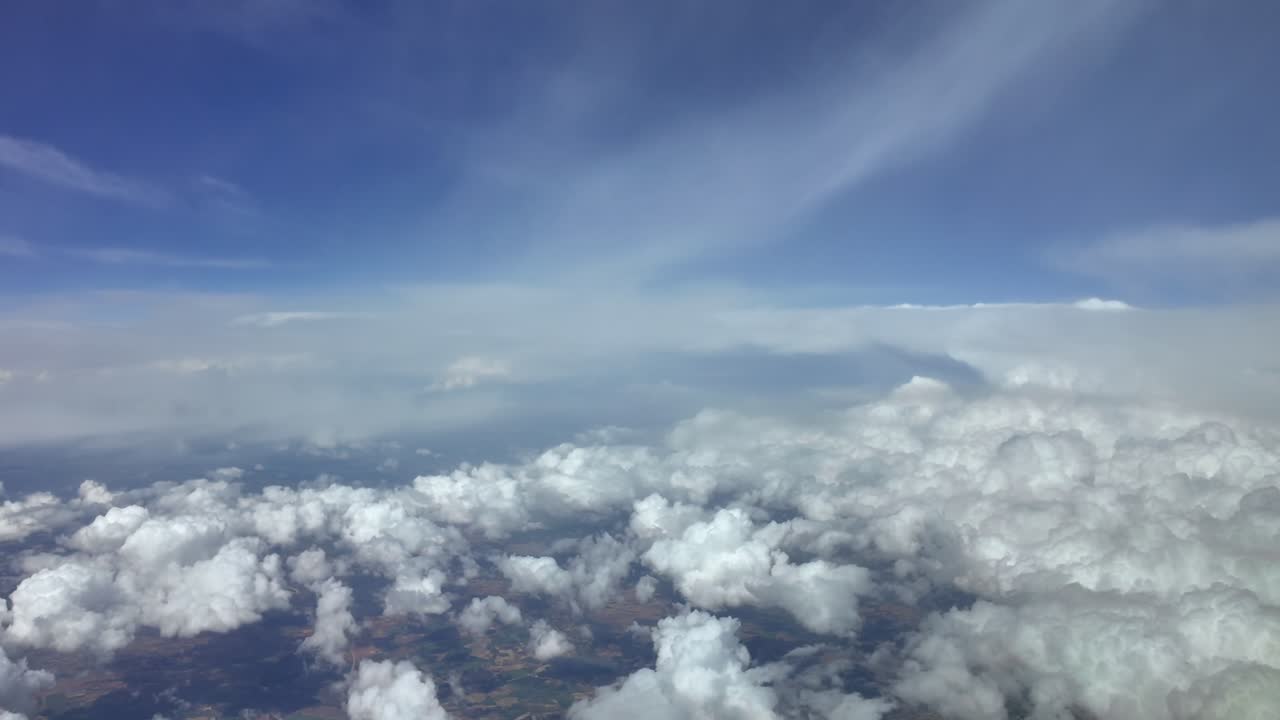 A High altitude flight perspective from a jet cockpit flying over stormy skies full of cottony clouds, under a deep blue sky.