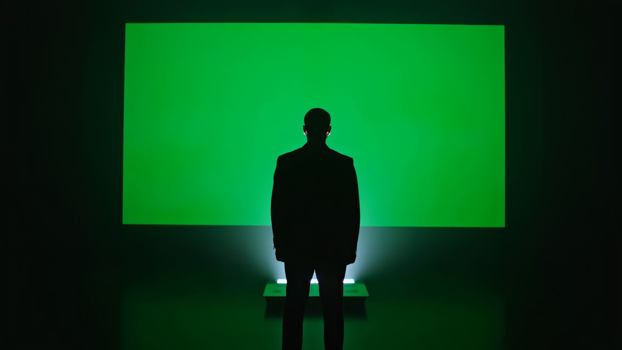Silhouette Man Stands Before Green Screen, Backlit Rim Highlights Suit Profile, Small Platform And Studio