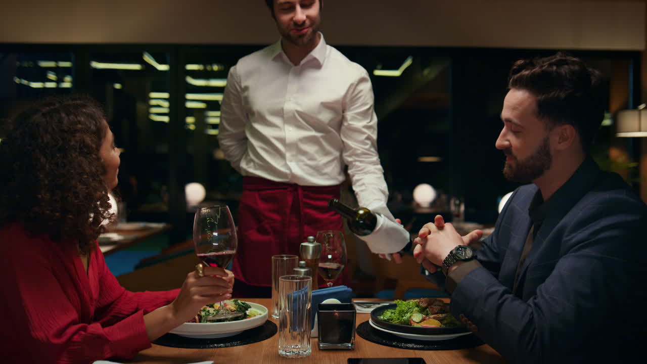 el camarero sirve vino a una pareja romántica en el restaurante. los amantes disfrutan de la bebida.