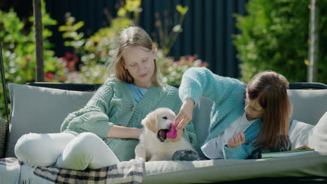 two girls playing with a puppy, sitting on a swing in the backyard of the house