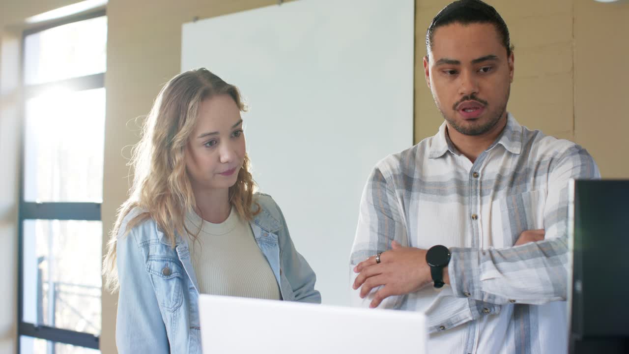 Diverse coworkers hearing initial remarks leaning forward and pointing at laptop at desk in office