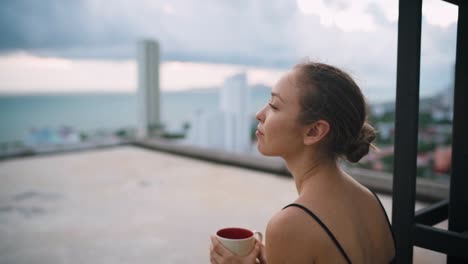 close up portrait shot of young woman sitting on roof and drinking coffee while looking to the side