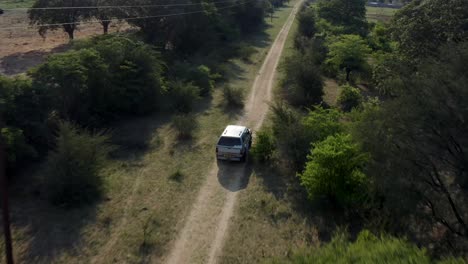 4x4 offroad vehicle driving on dirt track in african savanna, aerial