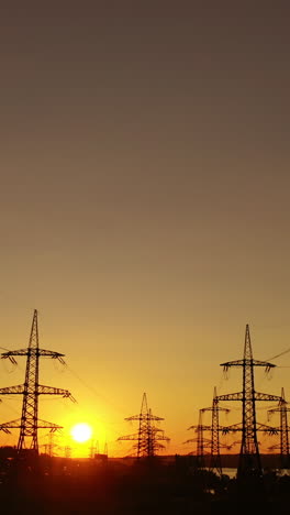 sunset among high voltage towers. transmission lines on the setting sun background. electricity distribution in the evening. motion camera back. vertical video