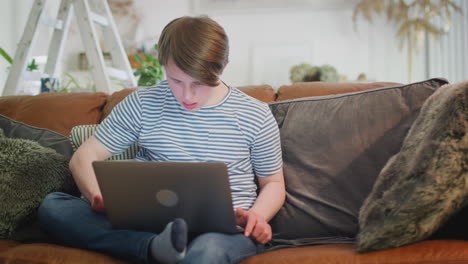 hombre con síndrome de down sentado en el sofá usando una computadora portátil en casa