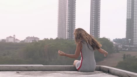 mujer con cabello oscuro se sienta en el techo contra el parque verde arbustivo