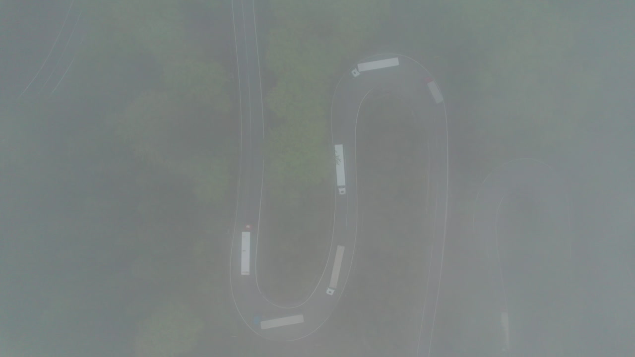 Trucks driving on winding roads in Romania, surrounded by trees and fog