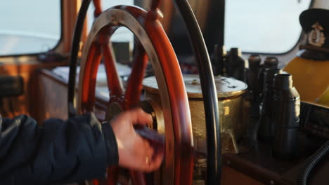 a person's hand on a classic ship's wooden steering wheel