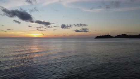 Taking-Off-Drone-Shot-Of-A-Sunset-By-The-Ocean-with-Island