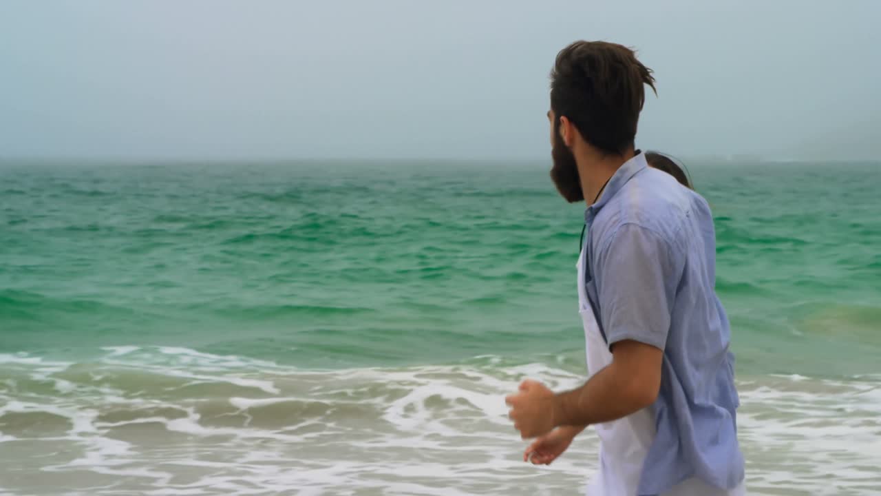 해변 4k에서 손을 잡고 달리는 백인 커플의 측면 뷰