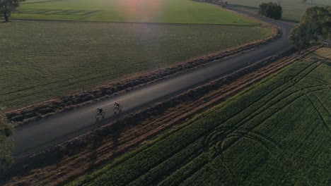 aerial view of 2 cyclist racing alone beautiful country roads with lush green crop field in the rural city of wagga wagga nsw australia
