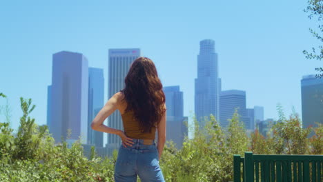 Unknown-brunette-looking-blurred-cityscape.-Young-woman-stand-in-public-garden