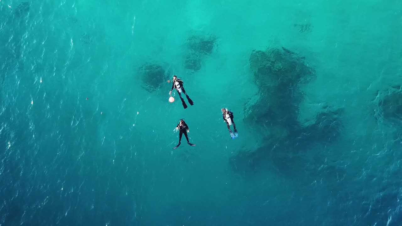 Aerial shot of three scuba divers floating in the ocean, Solomon Islands