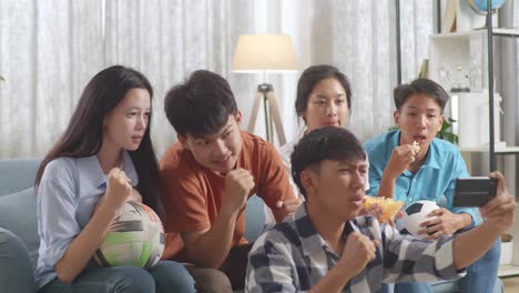 asian teenagers cheering and watching football game on smart phone at home