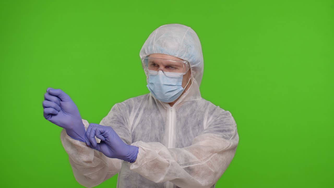 Healthcare worker doctor standing on chroma key and puts on gloves and mask, coronavirus pandemic