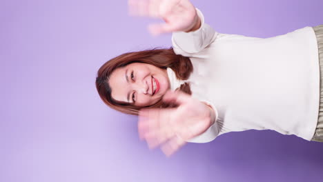 retrato vertical de una mujer asiática feliz saludando a la cámara y haciendo gestos de saludo mientras está aislada sobre un fondo violeta