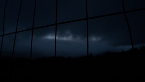 looking through metal fence into dark night sky, moving clouds during nightfall, dark silhouette
