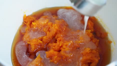 coconut milk being poured into roasted pumpkin puree in bowl preparing ingredients for muffins