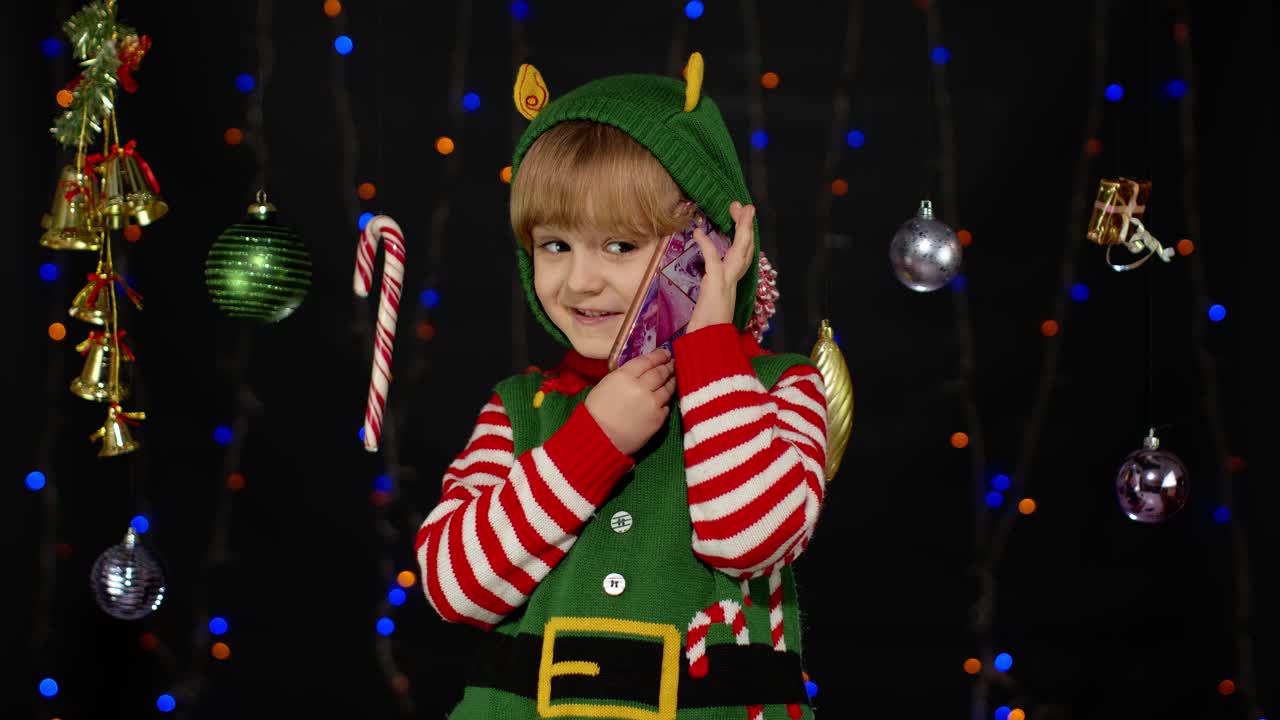 Kid girl in Christmas elf Santa Claus helper costume making congratulations call on mobile phone