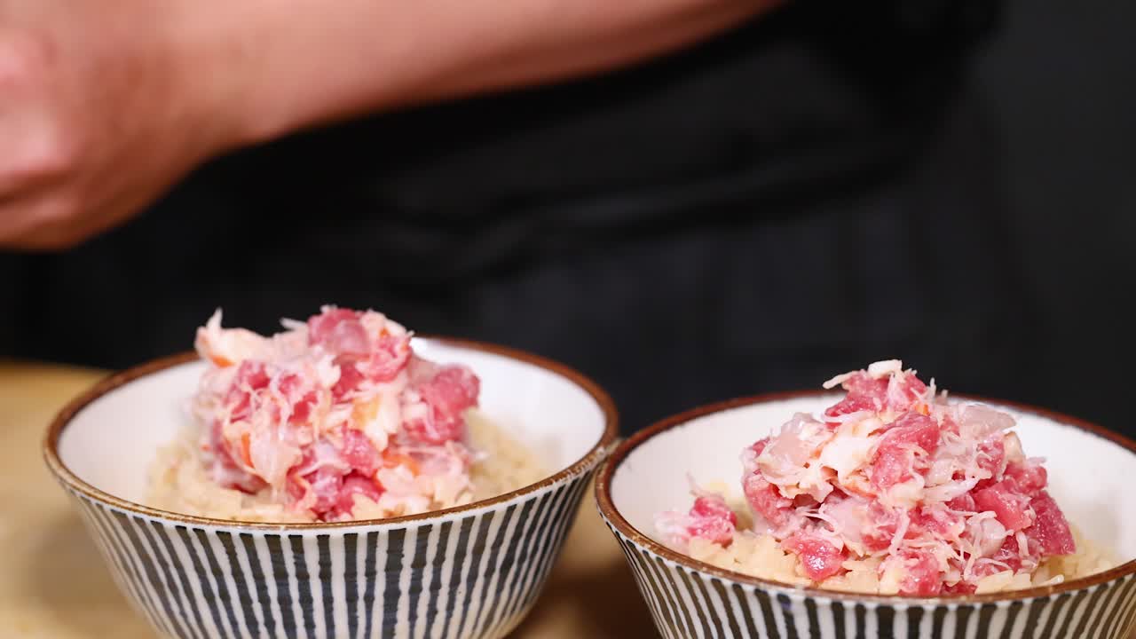 Primo piano di uno chef che, con dei cucchiai, posiziona con cura polpa di granchio fresca su ciotole di riso