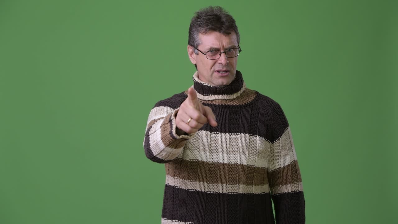 hombre guapo maduro con suéter de cuello alto contra un fondo verde