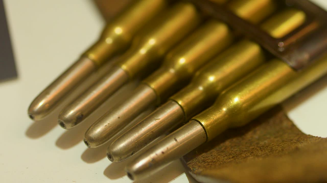 Brass rifle cartridges in clip, warm lighting, slow horizontal pan, museum display setting