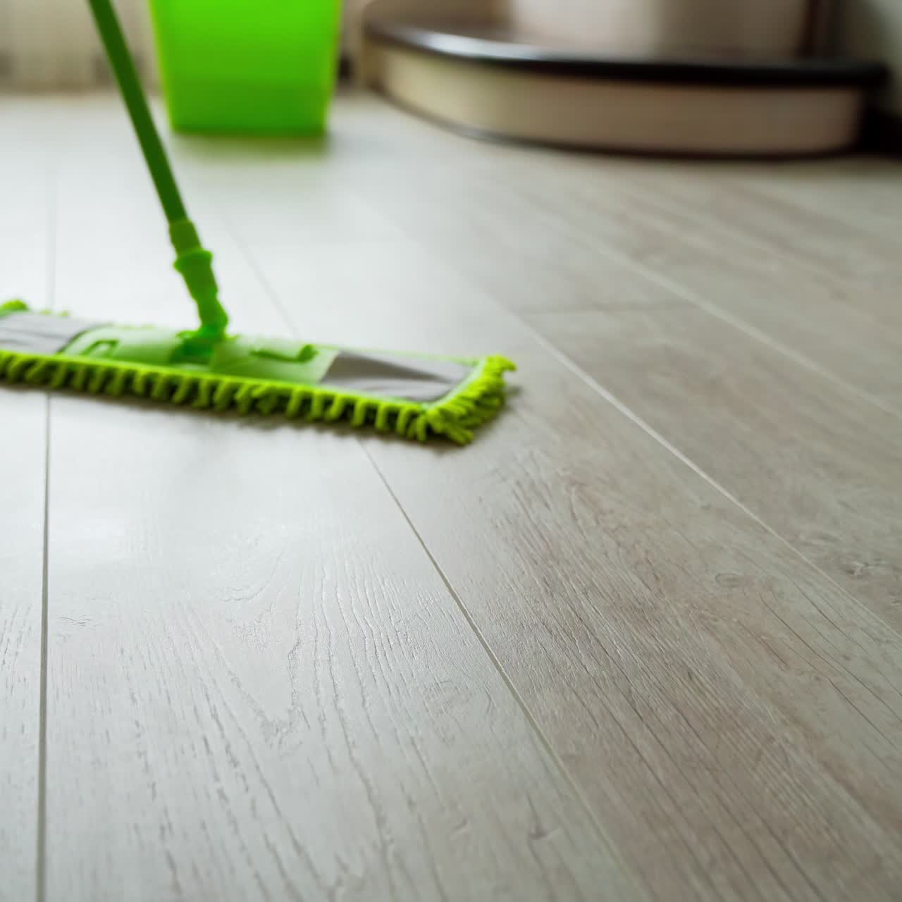 Cleaning parquet floors in the living room. Green mop cleaning the home floor. Householding duties. Close-up.