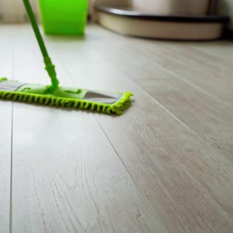 cleaning parquet floors in the living room. green mop cleaning the home floor. householding duties. close-up.