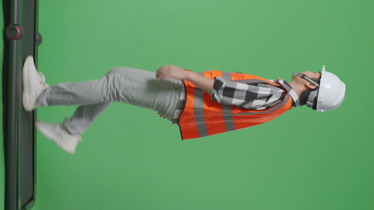 vista lateral de cuerpo completo ingeniero masculino asiático con casco de seguridad agitando la mano mientras camina en el estudio de fondo de pantalla verde