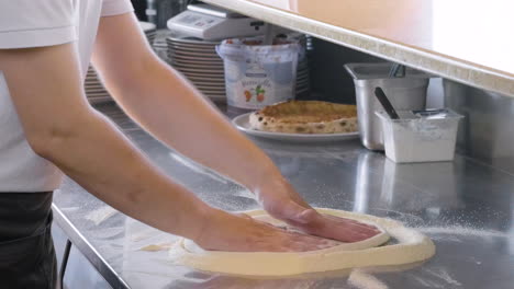 nahaufnahme eines nicht erkennbaren kochs, der pizzateig auf einer arbeitsplatte in einem restaurant knetet