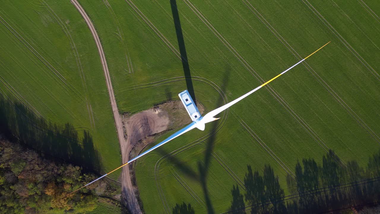 Wind turbine standing in green field next to highway autobahn in autumn Germany, generating renewable energy. Nice aerial view flight vertical bird's eye view drone rotation to left drone