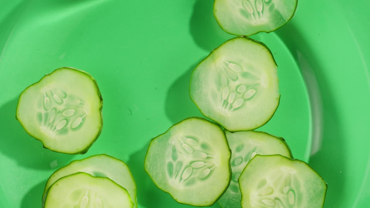 Cucumber slices rotate in splashes of juice on white background. High quality 4k footage