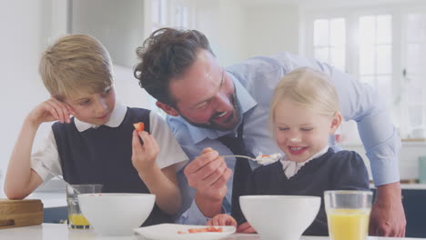 father wearing suit serving children in school uniform breakfast as he gets ready for work