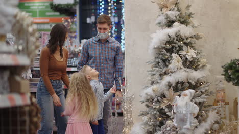 a happy family in medical masks in the store buys christmas decorations and gifts in slow motion