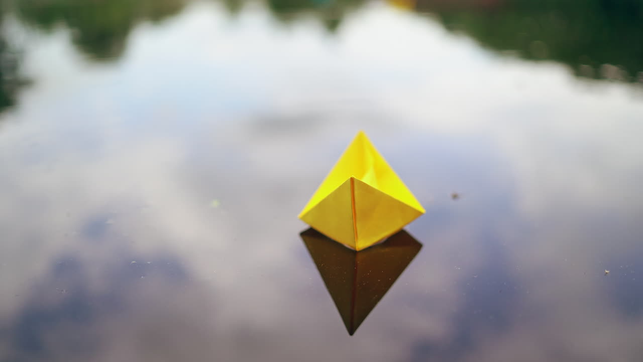 Woman's hand launches paper boat on the water. Paper boat sails along the river.