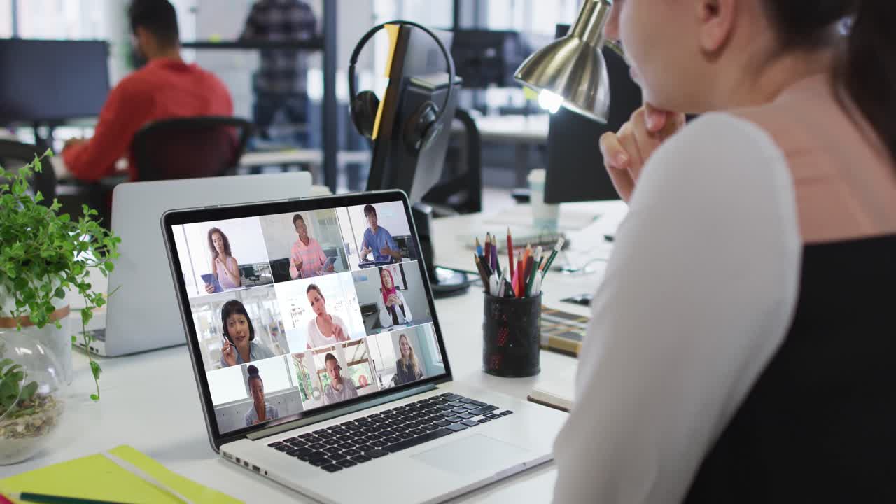 Kaukasisk kvinde deltager i videokonference med kontorkolleger på bærbar computer på kontoret.