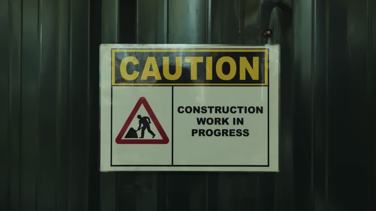 Closeup of caution sign warning about construction work in progress on metal wall