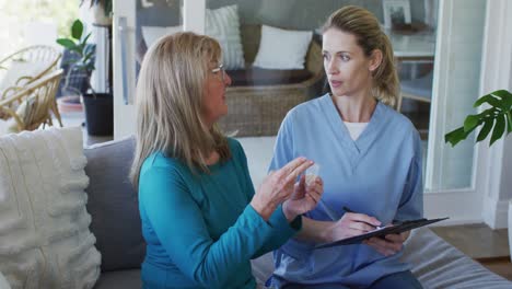 Senior-woman-holding-medication-container-talking-to-female-health-worker