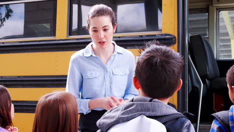 elementary school teacher and kids talking by school bus